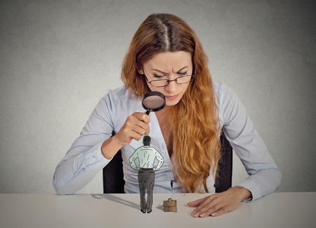 35516173 - curious corporate businesswoman skeptically meeting looking at small employee standing on table through magnifying glass isolated grey office wall background. human face expression attitude perception