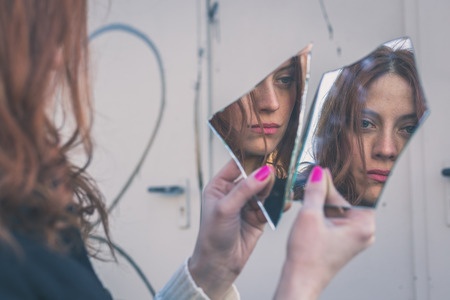39245451 - beautiful redhead girl with long hair and blue eyes looking at herself in a broken mirror