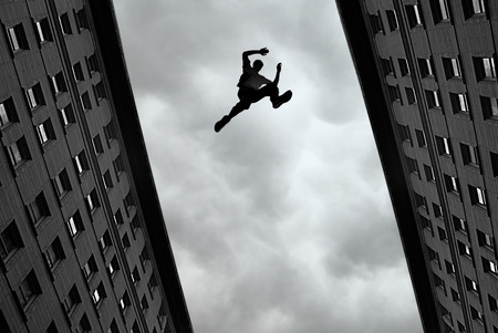 37963179 - man jumping over building roof against gray sky background